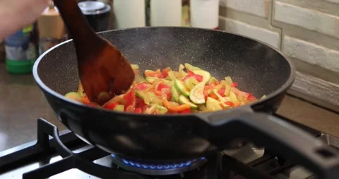 Chef mixes zucchini, tomatoes, cucumbers, sweet peppers and onions, fried in pan Stock Footage 218681831