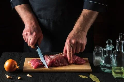 Chef or cook cutting beef meat with knife on kitchen, cooking food. Stock Photos