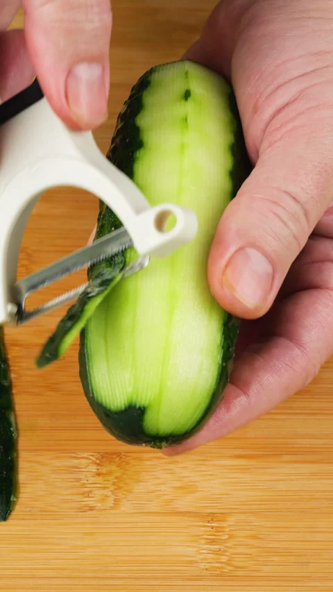 Chef peeling fresh green cucumber with white peeler over wooden cutting board. Video stock 341543037