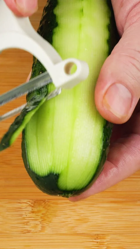 Chef peeling fresh green cucumber with white peeler over wooden cutting board. Video stock 342285402