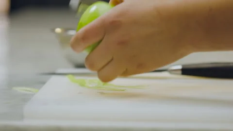 Chef peeling a green apple in close-up with out-of-focus utensils in the Stock Footage 321385023