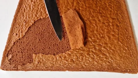Chef peeling the top layer of a fresh chocolate sponge cake with a metal knife Stock Footage 326633458