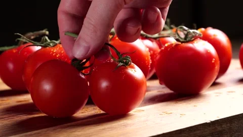 Chef picking two ripe red tomatoes from vine on wooden cutting board Stock Footage 305808524