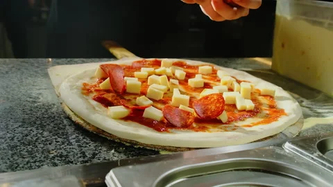 Chef places salami rounds between cheese cubes on sauced dough Stock Footage 325070942
