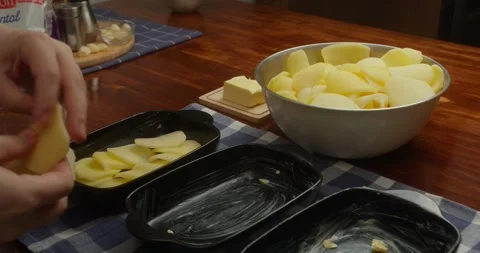 Chef places thinly sliced potatoes into cast iron baking dishes, arranging Vídeo Stock 327627386
