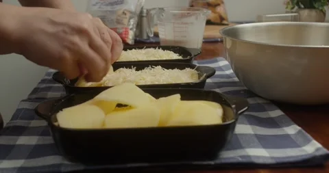 Chef places thinly sliced potatoes into cast iron baking dishes, arranging Vidéo 327627391