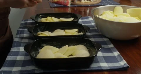 Chef places thinly sliced potatoes into cast iron baking dishes, arranging Vídeo Stock 327968039