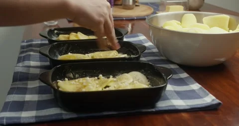 Chef places thinly sliced potatoes into cast iron baking dishes, arranging Vídeo Stock 330133632