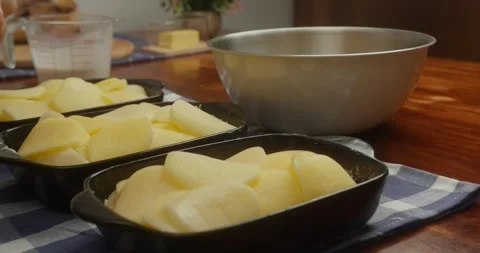 Chef places thinly sliced potatoes into cast iron baking dishes, arranging Видео 331283077