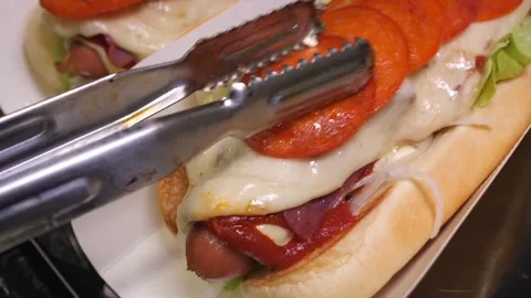 Chef placing fried pepperoni slices on cheese covered gourmet hot dogs Stock Footage 324711374