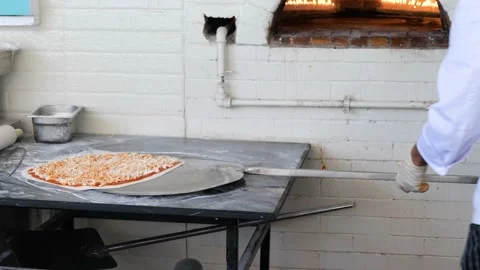 Chef Placing Pizza in fired oven in restaurant Stock Footage 153613114
