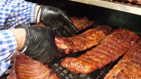 Chef placing a rack of smoky, slow-cooked BBQ ribs onto a hot grill at an outdoo 스톡 동영상 332813656