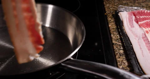 Chef placing a rasher of raw bacon into a frying pan Stock Footage 153747766