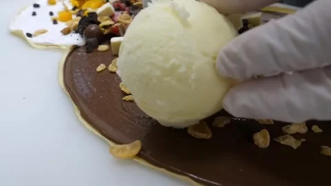 Chef placing a scoop of vanilla ice cream onto a chocolate crepe Stock Footage 345654579