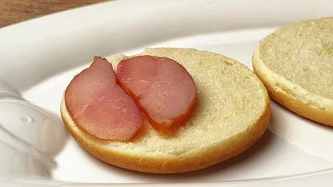 Chef placing smoked meat slices on a fresh burger bun for sandwich preparation Stock Footage 325032247