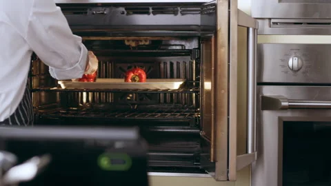 Chef placing tray of whole red peppers for roasting in oven in interior kitchen Stock Footage 199457658