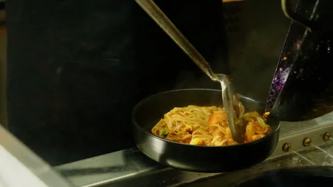 Chef plates pad thai noodles with tongs beside wok Video stock 324848111
