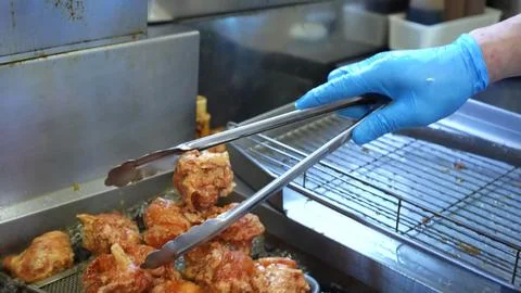 Chef plating crispy golden fried chicken pieces onto a metallic plate Stock Photos
