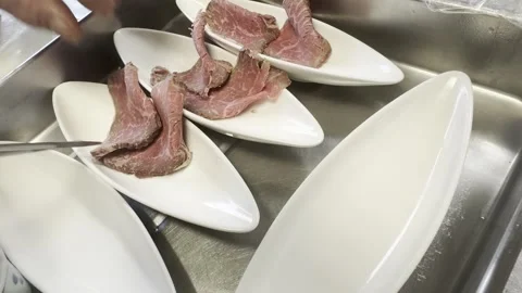 Chef Plating Slices Of Roast Beef On White Boat Shaped Dishes In A Kitchen Stock-Footage 338363298
