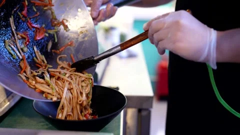 Chef plating stir-fried noodles with vegetables and chicken into a black bowl  Stock Footage 310929871