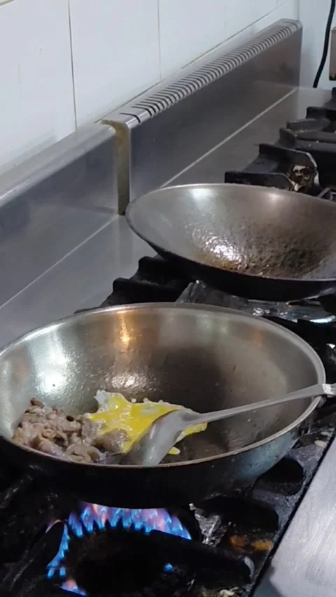 Chef pouring beaten egg into wok pan with meat on gas stove flame Stock Footage 340011655