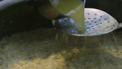 Chef pouring broth from large metal ladle over Uzbek plov in huge ancient kazan Stock Footage 332904700