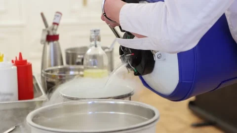 A chef is pouring liquid nitrogen from special barrel into steel bowl Stock Footage 189908364