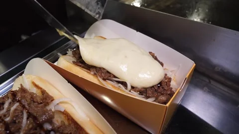Chef pouring melted cheese and sauteed beef on toasted buns for sandwiches Stock Footage 324713471