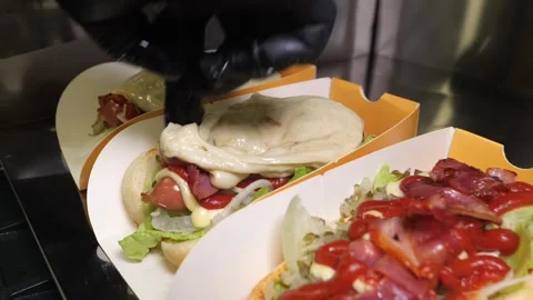 Chef pouring melted raclette cheese over a gourmet hot dog with bacon and sauce Stock Footage 324711152