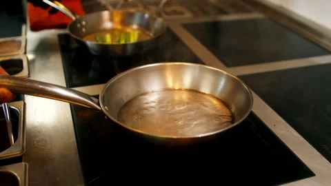 Chef pouring oil or liquid into a hot frying pan on a professional kitchen Stock Footage 337183377