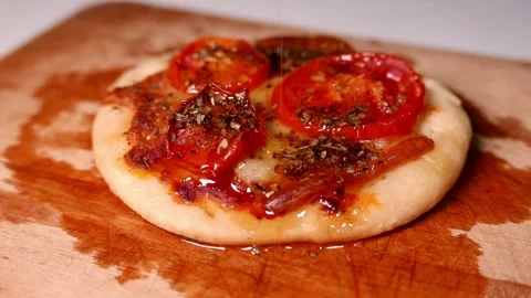 Chef pouring olive oil over a pizza topped with tomato, mozzarella, and oregano Stock Footage 345115084