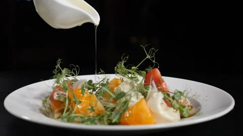 Chef pouring sauce on fresh vegetable salad on black background. close-up. Cook 스톡 동영상 122134476
