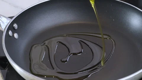 A chef pours a large amount of olive oil into a frying pan. Slow motion 100fps. Stock Footage 303406524