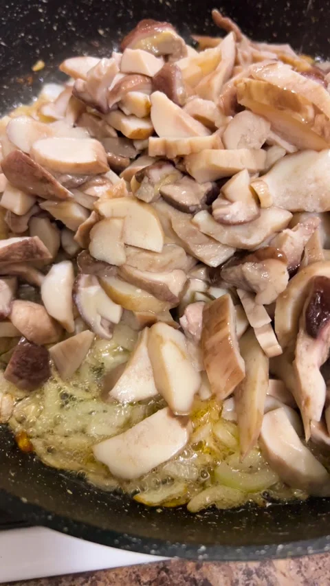 A chef pours a large portion of chopped porcini mushrooms into a frying pan. Stock-Footage 344184278