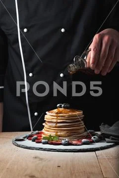 The chef pours maple syrup on pancake stack with blueberries and strawberries Stock Photos