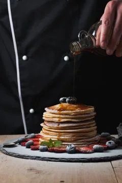 The chef pours maple syrup on pancake stack with blueberries and strawberries on Stock Photos