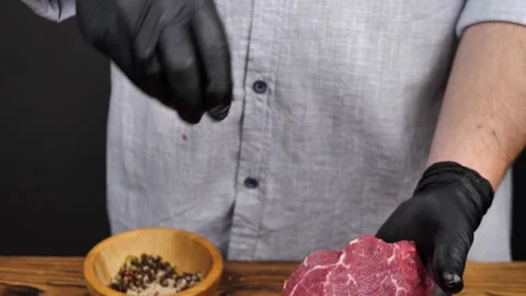 Chef pours a mixture of salt and pepper onto a beef steak on a wooden table. Stock Footage 261099998