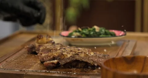 Chef pours salt on a soft baked grilled BBQ meat ribs on a wooden board. Meat Stock Footage 293786663