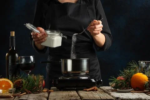 Chef pours sugar into pan for preparing mulled wine on rustic wooden table wi Stock Photos
