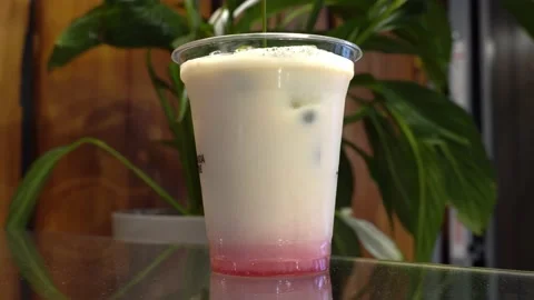 The chef pours tea into milk with raspberry syrup and ice on a green background Stock Footage 161603519