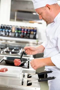 Chef prepares beef steak in pan at the kitchen Stock Photos