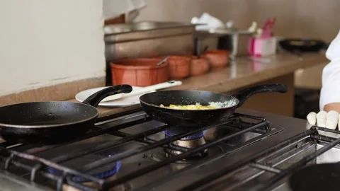 Chef prepares delicious scrambled eggs in frying pan on stove in restaurant Stock Footage 306055124