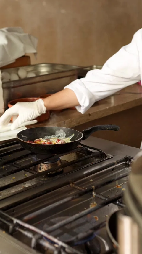 Chef prepares delicious scrambled eggs in frying pan on stove in restaurant Stock Footage 306543945