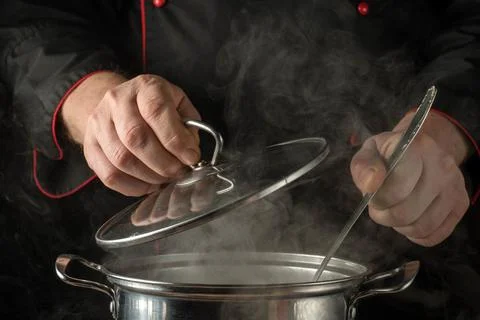 Chef prepares a dish by lifting the lid of a pot in a kitchen filled with s.. Stock Photos