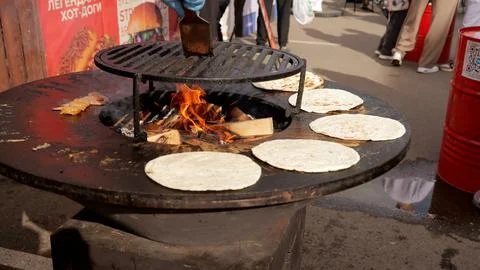 Chef prepares flatbread on circular outdoor wood fired grill during sunny street 스톡 사진