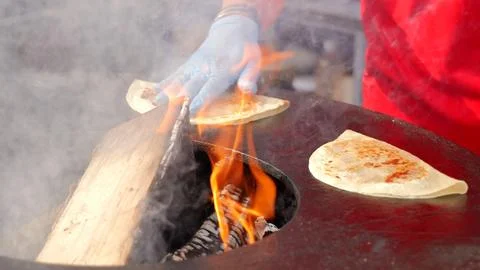Chef prepares flatbread on hot circular griddle over burning logs. Gloved hand Stockfoto's