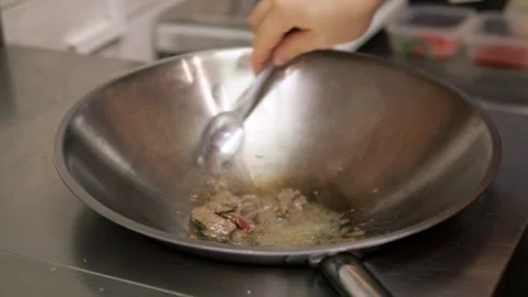A chef prepares fried pieces of meat, peppers in a huge wok in a restaurant - a Stockbeeldmateriaal 147654166
