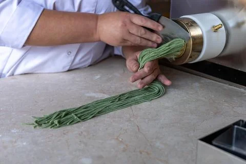 Chef prepares green noodles using a pasta machine in a trendy kitchen at a Stock Photos