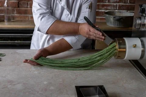 Chef prepares green noodles using a pasta machine in a trendy kitchen at a Stock Photos