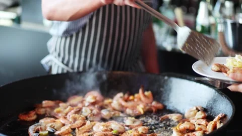 Chef prepares large batch of shrimp on grill in lively kitchen setting during Stock Footage 309892306